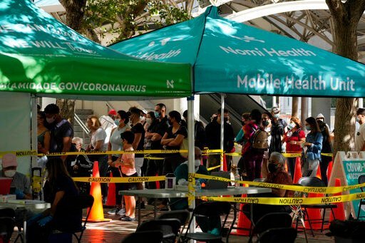FILE - Dozens of people wait in line to be tested for COVID-19, alongside other tents with no line where healthcare workers wait to administer vaccines, at a mobile health unit run by Nomi Health, Tuesday, Dec. 28, 2021, in downtown Miami. More than a year after the vaccine was rolled out, new cases of COVID-19 in the U.S. have soared to the highest level on record at over 265,000 per day on average, a surge driven largely by the highly contagious omicron variant. (AP Photo/Rebecca Blackwell, File)    PHOTO CREDIT: Rebecca Blackwell