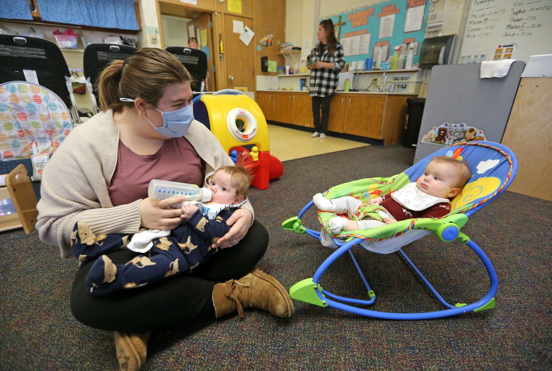 Holly Peterson, a child care associate at Holy Ghost Early Childhood Center, feeds Owen Sears, 4 months, while Mason Pudlo, 5 months, watches on Thursday at the center in Dubuque.    PHOTO CREDIT: JESSICA REILLY