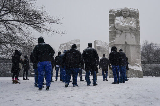 Visitors look to the Martin Luther King, Jr. Memorial as snow falls in Washington, Sunday, Jan. 16, 2022. Ceremonies scheduled for the site on Monday, to mark the Martin Luther King, Jr. national holiday, have been canceled because of the weather. (AP Photo/Carolyn Kaster)    PHOTO CREDIT: Carolyn Kaster