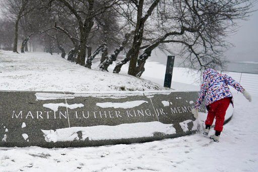 Shelby Batch, 12, of California, clears snow from the Martin Luther King, Jr. Memorial in Washington, Sunday, Jan. 16, 2022. Ceremonies scheduled for the site on Monday, to mark the Martin Luther King, Jr. national holiday, have been canceled because of the weather. (AP Photo/Carolyn Kaster)    PHOTO CREDIT: Carolyn Kaster
