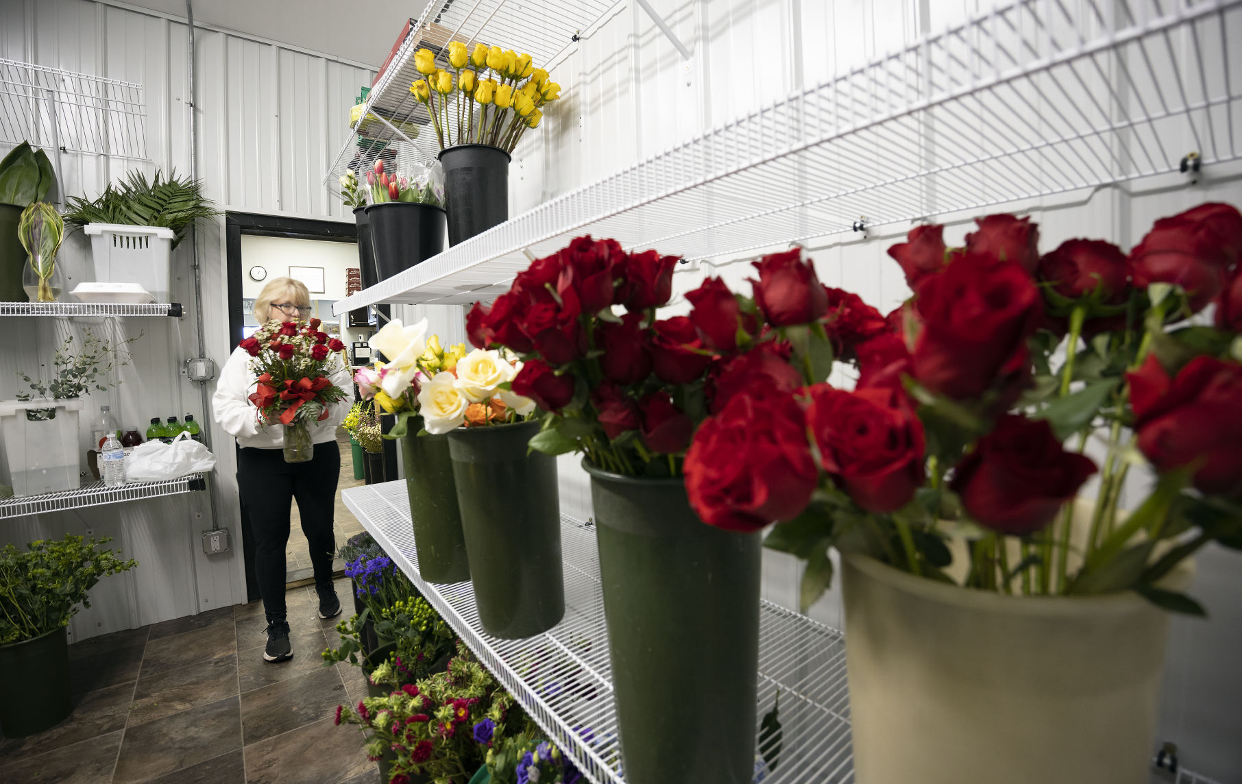Store manager Julie Gross carries a bouquet of roses into the cooler at Butt’s Florist in Dubuque on Friday.    PHOTO CREDIT: Stephen Gassman