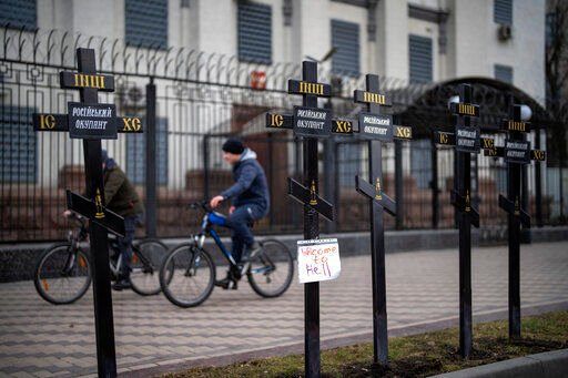 Cyclists ride past an installation of crosses on which is written "Russian occupier", in front of the Russian Embassy in Kyiv, Ukraine, Wednesday, Feb. 23, 2022. Ukraine urged its citizens to leave Russia as Europe braced for further confrontation Wednesday after Russia