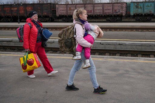 A woman carries a child while walking on a platform to board a Kyiv-bound train in Kostiantynivka, the Donetsk region, eastern Ukraine, Thursday, Feb. 24, 2022. Russia launched a wide-ranging attack on Ukraine on Thursday, hitting cities and bases with airstrikes or shelling, as civilians piled into trains and cars to flee. Ukraine