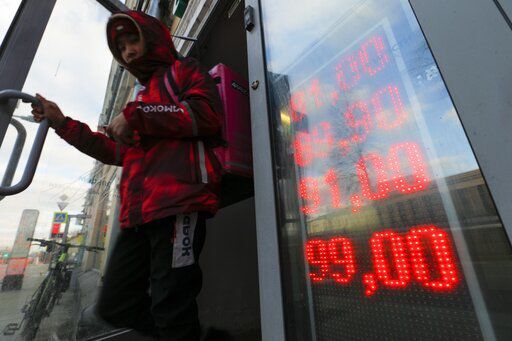 A food delivery man leaves an exchange office with screen showing the currency exchange rates of U.S. Dollar and Euro to Russian Rubles in Moscow, Russia. The ruble plunged to a record low of less than 1 U.S. cent in value today after Russia was cut off from the global bank payments system in retaliation for Moscow’s invasion of Ukraine.    PHOTO CREDIT: Alexander Zemlianichenko Jr