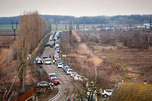 People walk next to a row of cars waiting to pick up family members and refugees fleeing the war in Ukraine, in Palanca, Moldova, Wednesday, March 2, 2022. Russian forces have escalated their attacks on crowded cities in what Ukraine