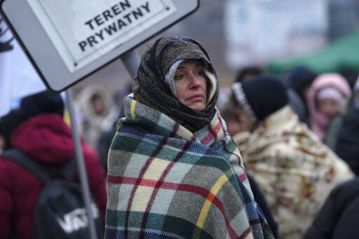 A woman wraps herself in a blanket to keep warm as she waits in a crowd of refugees after fleeing from the Ukraine and arriving at the border crossing in Medyka, Poland, Monday, March 7, 2022. Hundreds of thousands of Ukrainian civilians attempting to flee to safety Sunday were forced to shelter from Russian shelling that pummeled cities in Ukraine’s center, north and south. (AP Photo/Markus Schreiber)    PHOTO CREDIT: Markus Schreiber