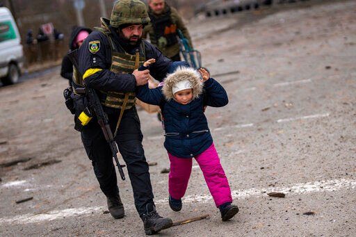 A Ukrainian police officer runs while holding a child as the artillery echoes nearby, while fleeing Irpin on the outskirts of Kyiv, Ukraine, Monday, March 7, 2022. Russia announced yet another cease-fire and a handful of humanitarian corridors to allow civilians to flee Ukraine. Previous such measures have fallen apart and Moscow