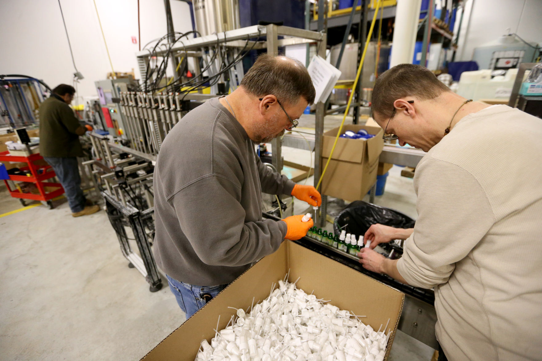 Gene Fangman (left) and Jeremy Crubaugh put caps on bottles at Higley Industries.    PHOTO CREDIT: JESSICA REILLY