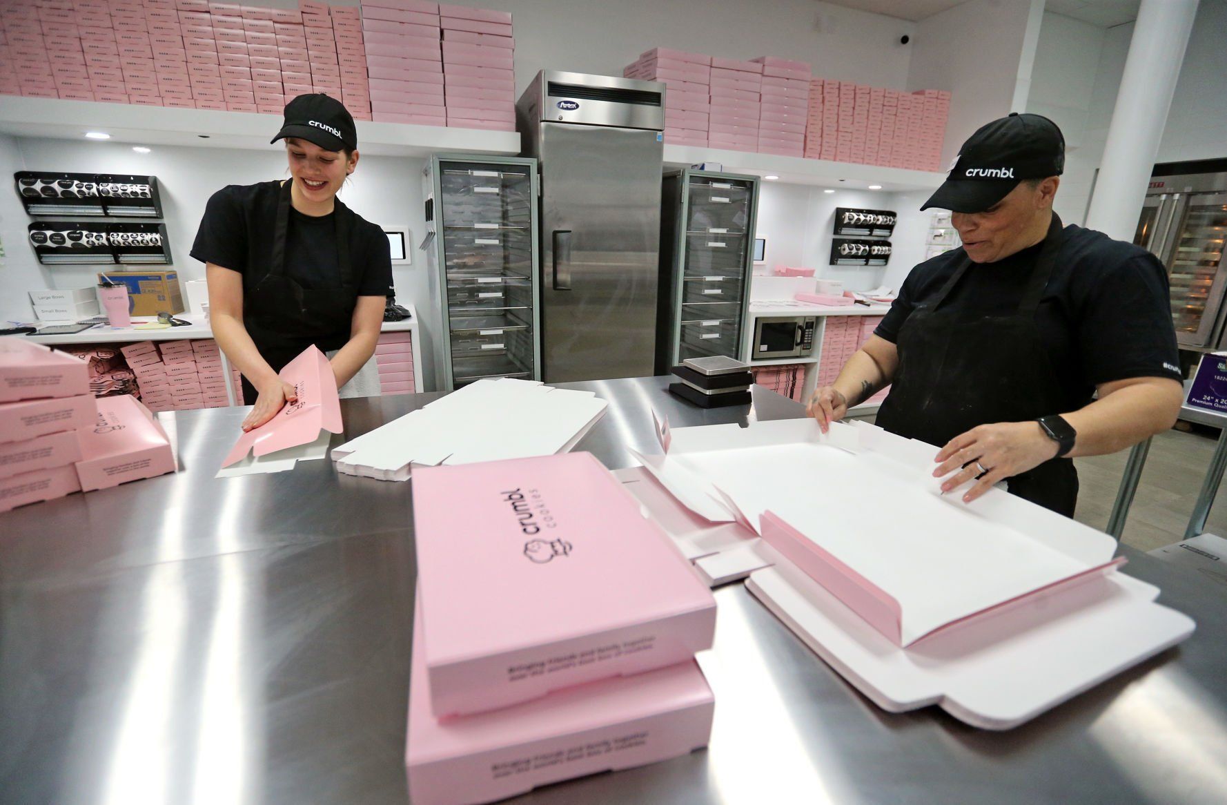 Cailyn Lord (left) and Claudette Irizarry make boxes at Crumbl Cookies in Dubuque on Wednesday, March 23, 2022. The store opens Friday, March 25.    PHOTO CREDIT: JESSICA REILLY