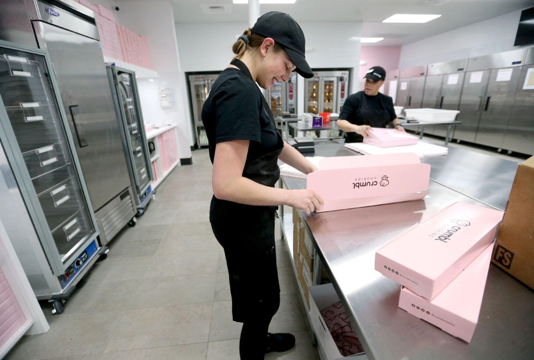 Cailyn Lord (left) and Claudette Irizarry make boxes at Crumbl Cookies in Dubuque on Wednesday, March 23, 2022. The store opens Friday, March 25.    PHOTO CREDIT: JESSICA REILLY