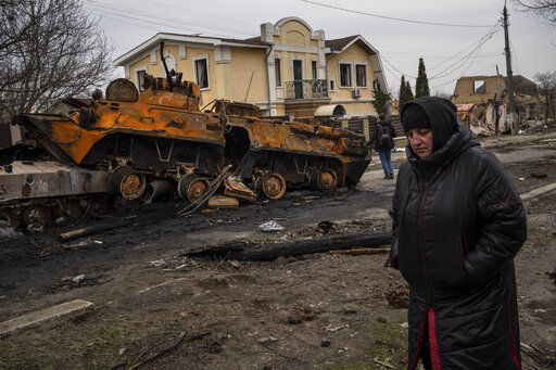 A woman walks next to a destroyed Russian armor vehicle in Bucha, in the outskirts of Kyiv, Ukraine, Tuesday, April 5, 2022. Ukraine’s president plans to address the U.N.’s most powerful body after even more grisly evidence emerged of civilian massacres in areas that Russian forces recently left. (AP Photo/Rodrigo Abd)    PHOTO CREDIT: Rodrigo Abd