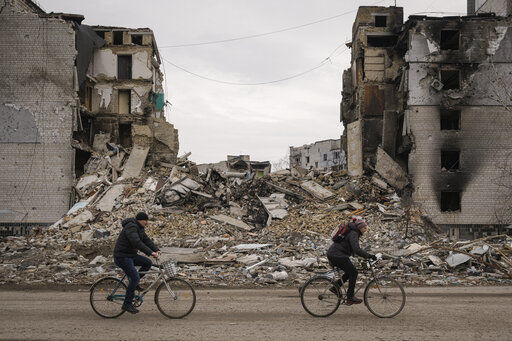 People ride bicycles by an apartment building destroyed during fighting between Ukrainian and Russian forces in Borodyanka, Ukraine, Tuesday, April 5, 2022. Ukrainian President Volodymyr Zelenskyy accused Russian troops of gruesome atrocities in Ukraine and told the U.N. Security Council on Tuesday that those responsible should immediately be brought up on war crimes charges in front of a tribunal like the one set up at Nuremberg after World War II.(AP Photo/Vadim Ghirda)    PHOTO CREDIT: Vadim Ghirda