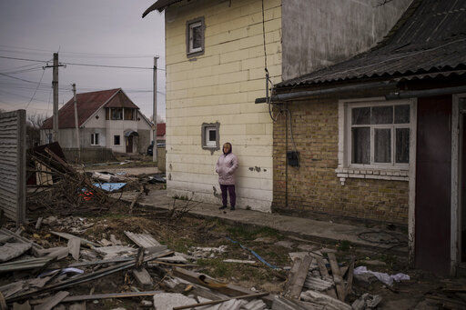 A woman watches as workers remove the bodies of three men killed in Bucha, outskirts of Kyiv, Ukraine, Tuesday, April 5, 2022. Ukraine’s president plans to address the U.N.’s most powerful body after even more grisly evidence emerged of civilian massacres in areas that Russian forces recently left. (AP Photo/Felipe Dana)    PHOTO CREDIT: Felipe Dana