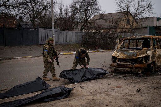 Ukrainian soldiers recover the remains of four killed civilians from inside a charred vehicle in Bucha, Ukraine. Western governments prepared today to toughen sanctions against Russia and send more weapons to Ukraine, after President Volodymyr Zelenskyy pointedly accused the world of failing to end Moscow’s invasion of his country and what he said was a campaign of murders, rapes and wanton destruction by Russian forces.    PHOTO CREDIT: Felipe Dana