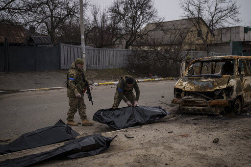 Ukrainian soldiers recover the remains of four killed civilians from inside a charred vehicle in Bucha, outskirts of Kyiv, Ukraine, Tuesday, April 5, 2022. Ukraine’s president plans to address the U.N.’s most powerful body after even more grisly evidence emerged of civilian massacres in areas that Russian forces recently left. (AP Photo/Felipe Dana)    PHOTO CREDIT: Felipe Dana