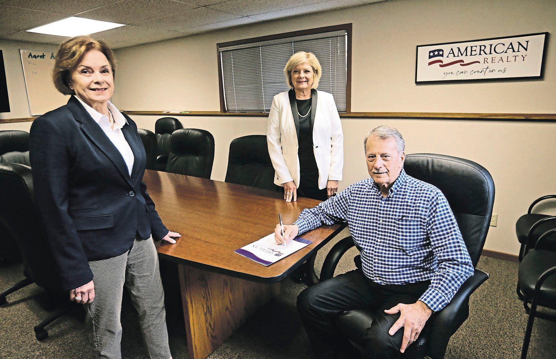 Peggy Nesler (from left), Shari Greenwood and Robert Neuwoehner gather in a boardroom at American Realty. Neuwoehner and Jim Curoe started it in Dubuque in 1972. Today, Nesler and Greenwood are at the helm as it celebrates its 50th anniversary.    PHOTO CREDIT: JESSICA REILLY