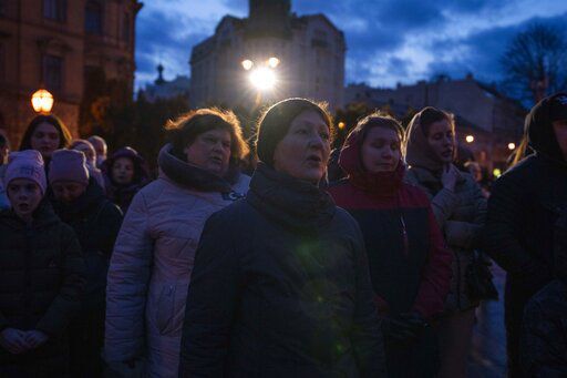 People listen to prayers before lighting candles forming Ukraine