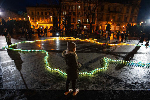 A girl stands in front of lit candles forming the shape of Ukraine