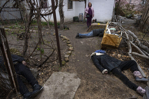A woman stands next to three men killed in the courtyard of a house in Bucha, in the outskirts of Kyiv, Ukraine, Tuesday, April 5, 2022. (AP Photo/Rodrigo Abd)    PHOTO CREDIT: Rodrigo Abd
