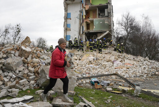 A woman carries her belongings as she leaves her house, background, ruined in the Russian shelling in Borodyanka, Ukraine, Wednesday, April 6, 2022. (AP Photo/Efrem Lukatsky)    PHOTO CREDIT: Efrem Lukatsky