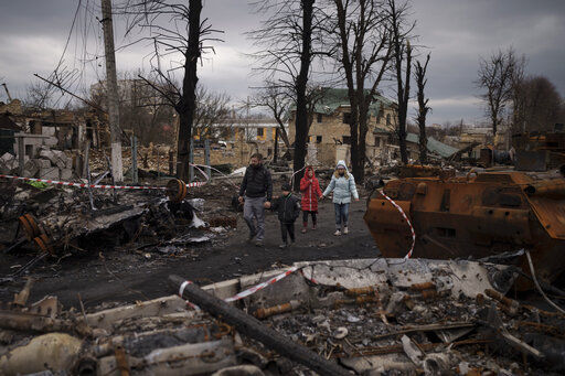 A family walks amid destroyed Russian tanks in Bucha, on the outskirts of Kyiv, Ukraine, Wednesday, April 6, 2022. (AP Photo/Felipe Dana)    PHOTO CREDIT: Felipe Dana