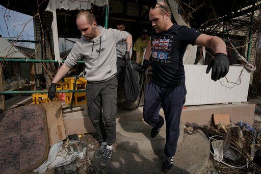 Municipal workers remove the body of a man from a house in Bucha, Ukraine, Thursday, April 7, 2022. Russian troops left behind crushed buildings, streets littered with destroyed cars and residents in dire need of food and other aid in a northern Ukrainian city, giving fuel to Kyiv