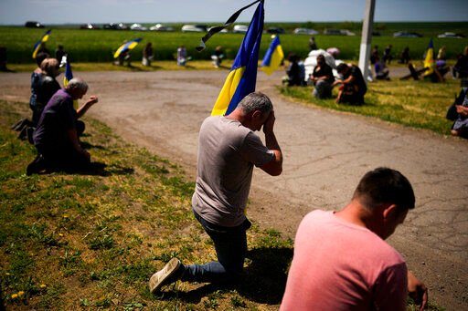 Mourners kneel as they await the coffin of Volodymyr Losev, 38, to pass by during his funeral in Zorya Truda, Odesa region, Ukraine, Monday, May 16, 2022. Volodymyr Losev, a Ukrainian volunteer soldier, was killed May 7 when the military vehicle he was driving ran over a mine in eastern Ukraine. (AP Photo/Francisco Seco)    PHOTO CREDIT: Francisco Seco