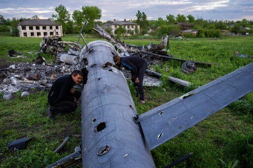 Roman Voitko (left) and Oleksiy Polyakov check the remains of a destroyed Russian helicopter in a field in the village of Malaya Rohan, Kharkiv region, Ukraine, on Monday.    PHOTO CREDIT: Bernat Armangue