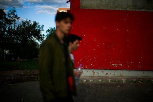 Youngsters walk past a wall scarred by shrapnel after a bombing earlier in the day in Mykolaiv, Ukraine, Monday, May 16, 2022. (AP Photo/Francisco Seco)    PHOTO CREDIT: Francisco Seco