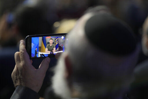 A man watches on his phone Ukrainian President Volodymyr Zelenskyy addressing the audience from Kyiv on a screen during the World Economic Forum in Davos, Switzerland, Monday, May 23, 2022. The annual meeting of the World Economic Forum is taking place in Davos from May 22 until May 26, 2022. (AP Photo/Markus Schreiber)    PHOTO CREDIT: Markus Schreiber