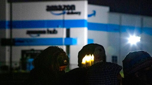 A person holds six electric candles symbolizing the six workers who died while working at the Edwardsville Amazon site in the background, during a vigil, Dec. 17, in Edwardsville, Ill., after part of the building collapsed due to a tornado the previous week before. Democratic members of the House Committee on Oversight and Reform are accusing Amazon of “obstructing” their investigation into the company