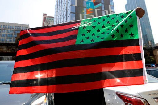 A man holds an African-American flag during a demonstration in Chicago on June 19, 2020, to mark Juneteenth, the holiday celebrating the day in 1865 that enslaved black people in Galveston, Texas, learned they had been freed from bondage, more than two years after the Emancipation Proclamation. Retailers and marketers from Walmart to Amazon have been quick to commemorate Juneteenth with an avalanche of merchandise from ice cream to T-shirts to party favors.     PHOTO CREDIT: Nam Y. Huh