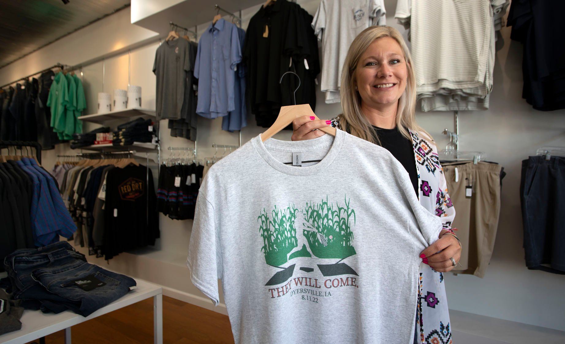 Jennifer Recker, owner of Haberdash Outfitters Co., shows off one of several Field of Dreams-themed shirts for sale at the business in Dyersville, Iowa, as the Chicago Cubs and Cincinnati Reds game approaches.    PHOTO CREDIT: Stephen Gassman