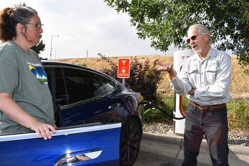 Jeannette Englehart of Billings, Mont. (left) stands outside her car speaking with fellow electric vehicle owner Bob Palrud of Spokane, Wash. at a charging station near Interstate 90, on Wednesday Sept. 14, 2022, in Billings, Mont. Officials from rural states in the U.S. west are pushing the Biden administration to ease requirements for charging stations because of limited demand in areas with low population densities. (AP Photo/Matthew Brown)    PHOTO CREDIT: Matthew Brown