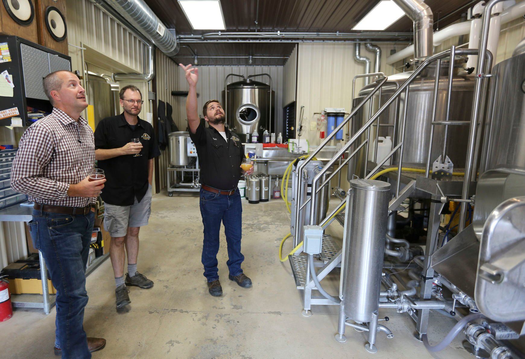 Iowa Secretary of Agriculture Mike Naig (left) listens to Franklin Street Brewing Co. brewmaster Matt Knutson (right) explain the brewing process during a tour of the facility in Manchester, Iowa, on Thursday. Company co-owner Kyle Sands also is pictured.    PHOTO CREDIT: Dave Kettering
