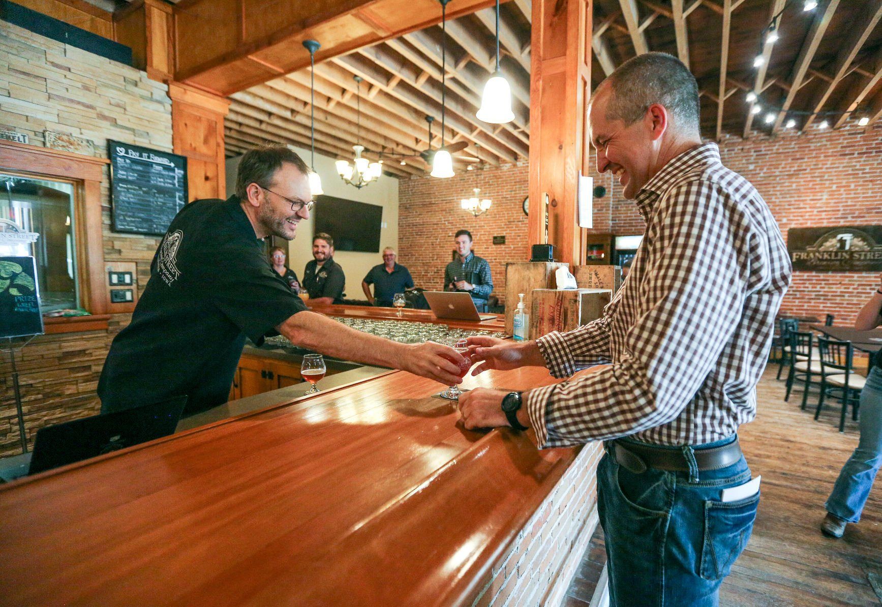 Franklin Street Brewing Company co-owner, Kyle Sands (left), serves up a sample of their product to Iowa Secretary of Agriculture Mike Naig who was in Manchester, Iowa on Thursday, Sept. 15 as part of his 99 county tour.    PHOTO CREDIT: Dave Kettering