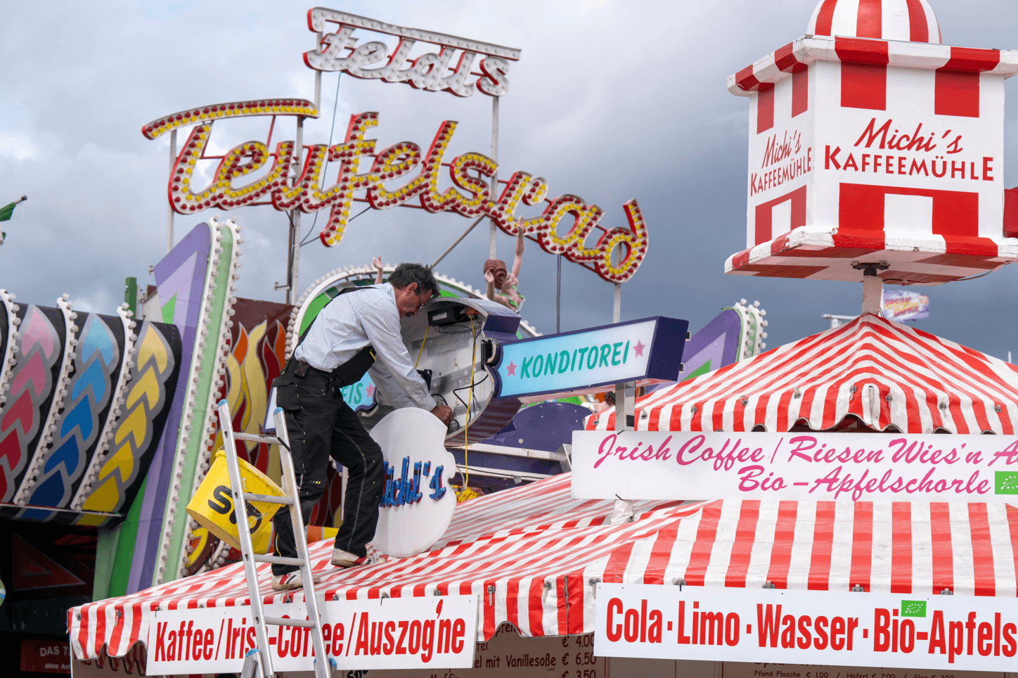 A man mounts a light advertisement on a booth on the Oktoberfest grounds in Munich, Germany, on Thursday. The Oktoberfest is on tap again in Germany after a two-year pandemic interruption. The beer will be just as cold and the pork knuckle just as juicy. But brewers and visitors are under pressure from inflation in ways they could hardly imagine in 2019.  