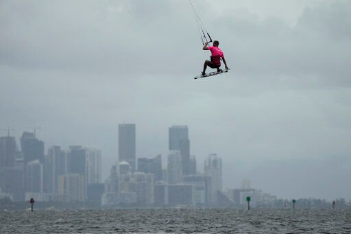 A man flies high with the Miami skyline in the background, as kite surfers take advantage of strong winds caused by distant Hurricane Ian, at Matheson Hammock Park in Coral Gables, Fla., Tuesday, Sept. 27, 2022. (AP Photo/Rebecca Blackwell)    PHOTO CREDIT: Rebecca Blackwell