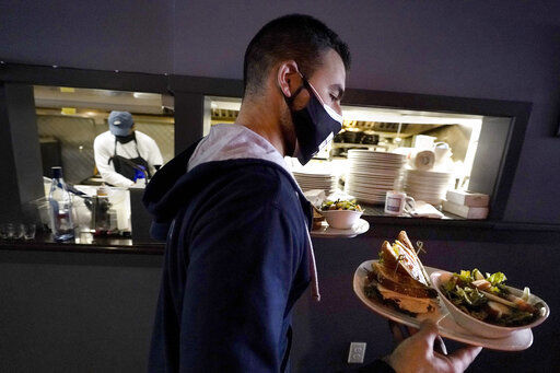 FILE - Bartender Denis Angelov carries plates of food from the kitchen, behind, at Tin Pan Alley restaurant, Tuesday, April 6, 2021, in Provincetown, Mass. The number of available jobs in the U.S. plummeted in August 2022 compared with July as businesses grow less desperate for workers, a trend that could cool chronically high inflation. (AP Photo/Steven Senne, File)    PHOTO CREDIT: Steven Senne