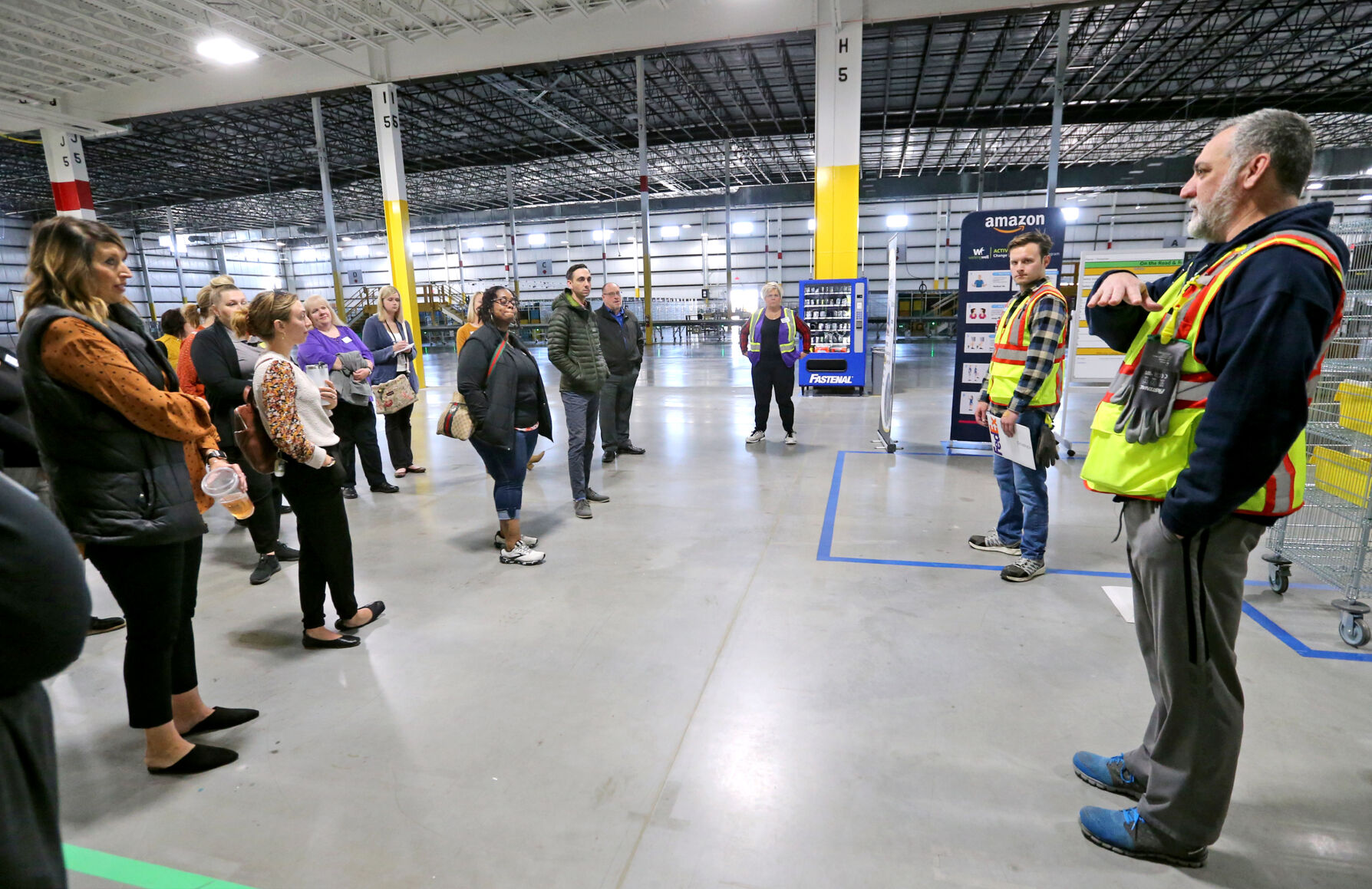 Rob Gruber (right) and Max Flynn (second from right), both managers at Amazon, give a tour of the facility in Dubuque on Thursday. Iowa Vocational Rehabilitation Services hosted a tour of local businesses that hire people with disabilities.    PHOTO CREDIT: JESSICA REILLY