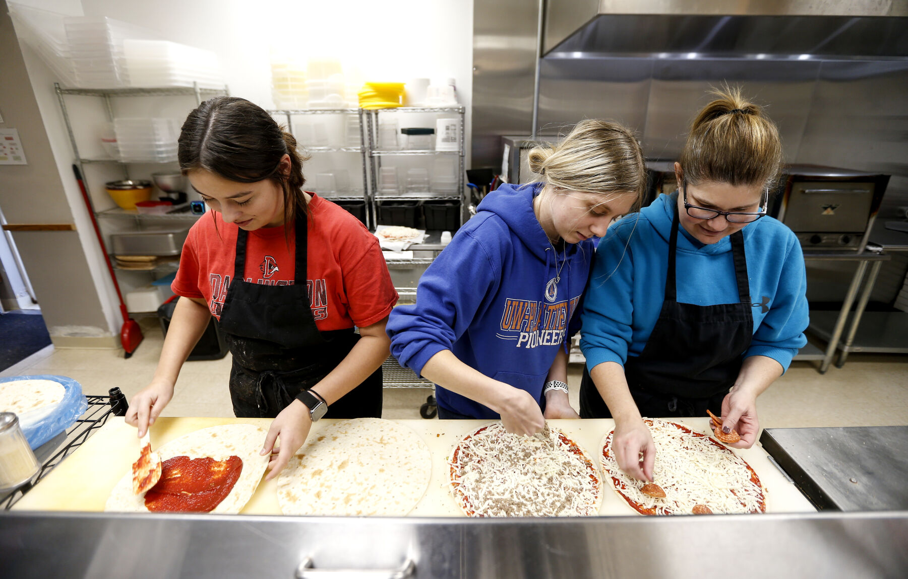 Alexis Mosley (left), 16, works with Ava Smith and her mother, co-owner Val Smith on making pizzas at Vinger’s Pizza in Darlington, Wis., before opening on Saturday, Nov. 26, 2022.    PHOTO CREDIT: Dave Kettering