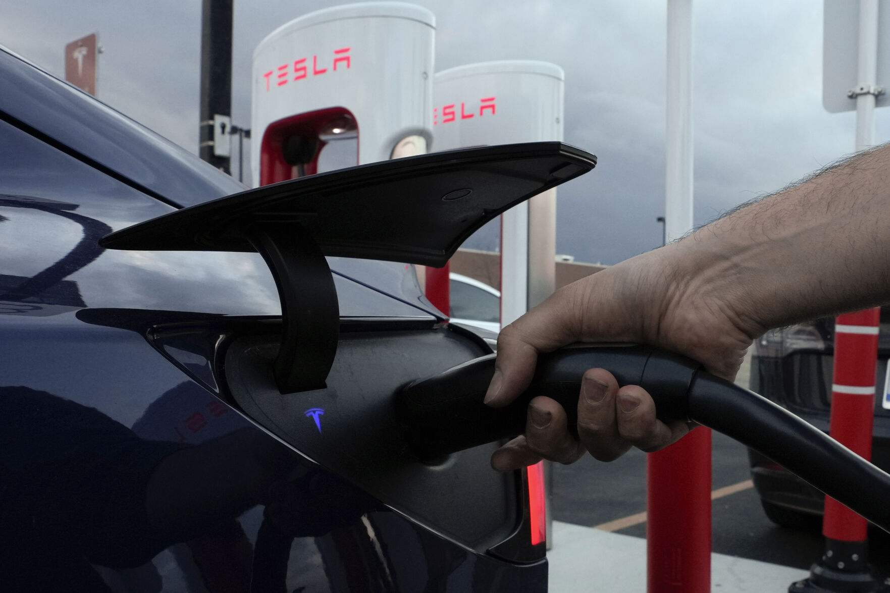 <p>FILE - A motorist charges his electric vehicle at a Tesla Supercharger station in Detroit, Wednesday, Nov. 16, 2022. About half of U.S. adults say they are not likely to go electric when it comes time to buy a new vehicle, a new poll by The Associated Press-NORC Center for Public Affairs Research and the Energy Policy Institute at the University of Chicago shows. (AP Photo/Paul Sancya, File)</p>   PHOTO CREDIT: Paul Sancya 