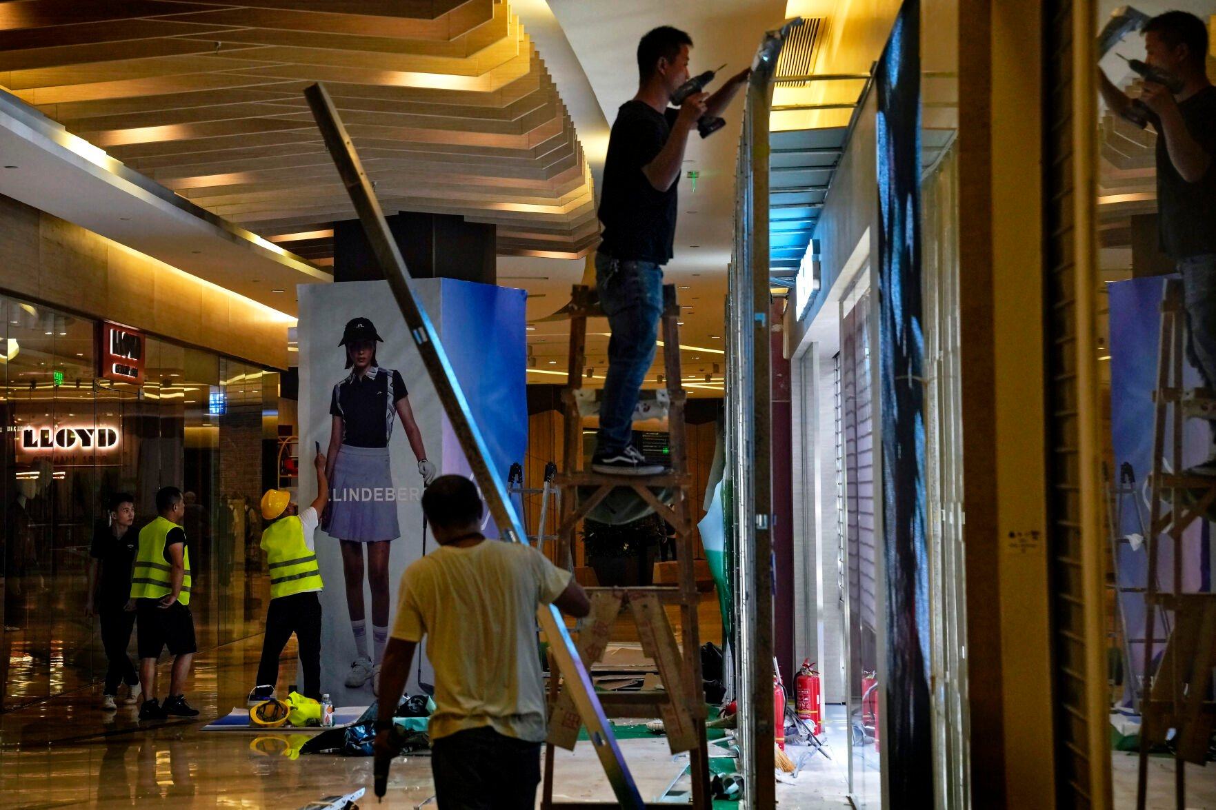 Workers install advertisement posters outside a new fashion boutique at a shopping mall in Beijing on Monday, Aug. 14, 2023. China’s government skipped giving an update on a politically sensitive spike in unemployment among young people as official data Tuesday, Aug. 15, showed an economic slump deepened in July. (AP Photo/Andy Wong)    PHOTO CREDIT: Associated Press