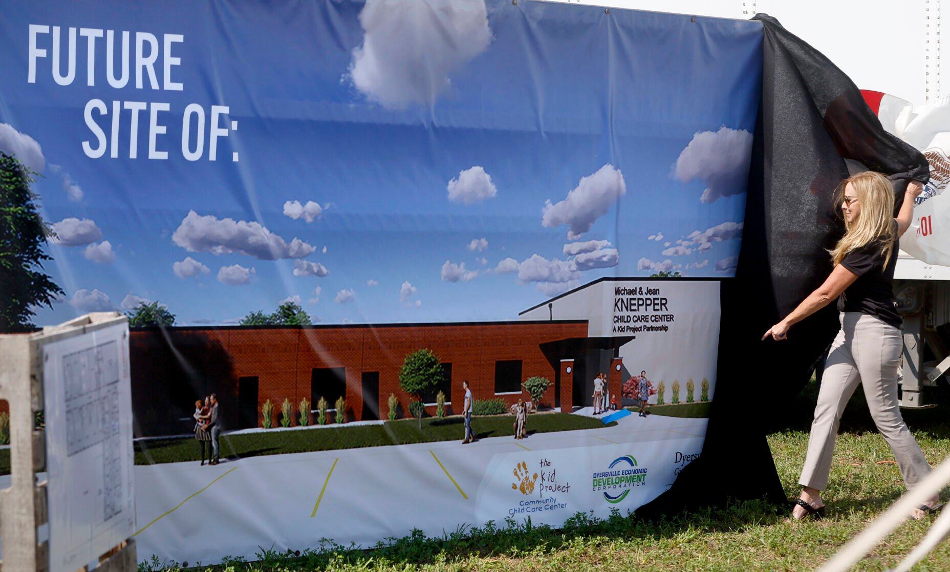 Dyersville Economic Development Corp. Executive Director Jacque Rahe unveils a banner on Thursday during a press conference at the future site of Michael and Jean Knepper Child Care Center in Dyersville, Iowa.    PHOTO CREDIT: JESSICA REILLY, Telegraph Herald
