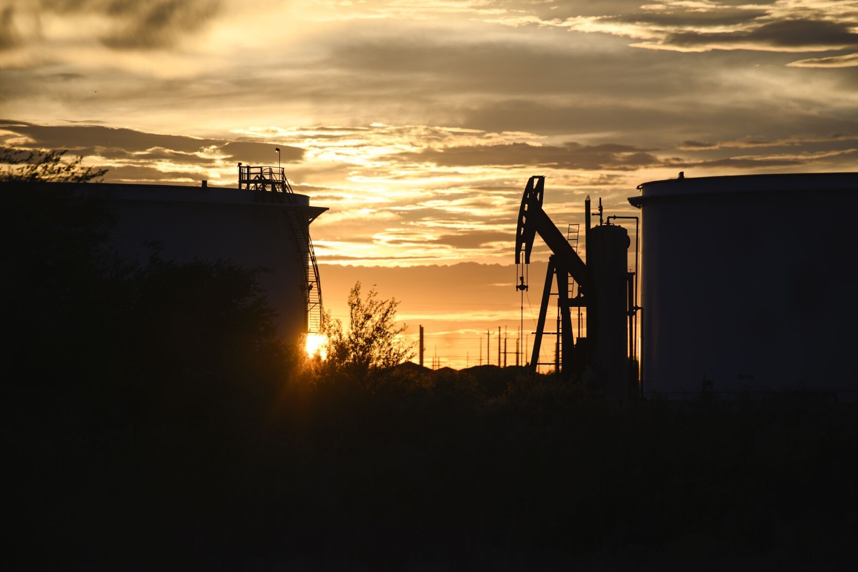 <p>FILE - The sun begins to set behind crude oil tanks and a pumpjack, July 5, 2022, in Midland, Texas. The IEA’s annual world energy outlook, which analyzes the global picture of energy supply and demand, was released Tuesday, Oct. 24, 2023. (Eli Hartman/Odessa American via AP, File)</p>   PHOTO CREDIT: Eli Hartman 
