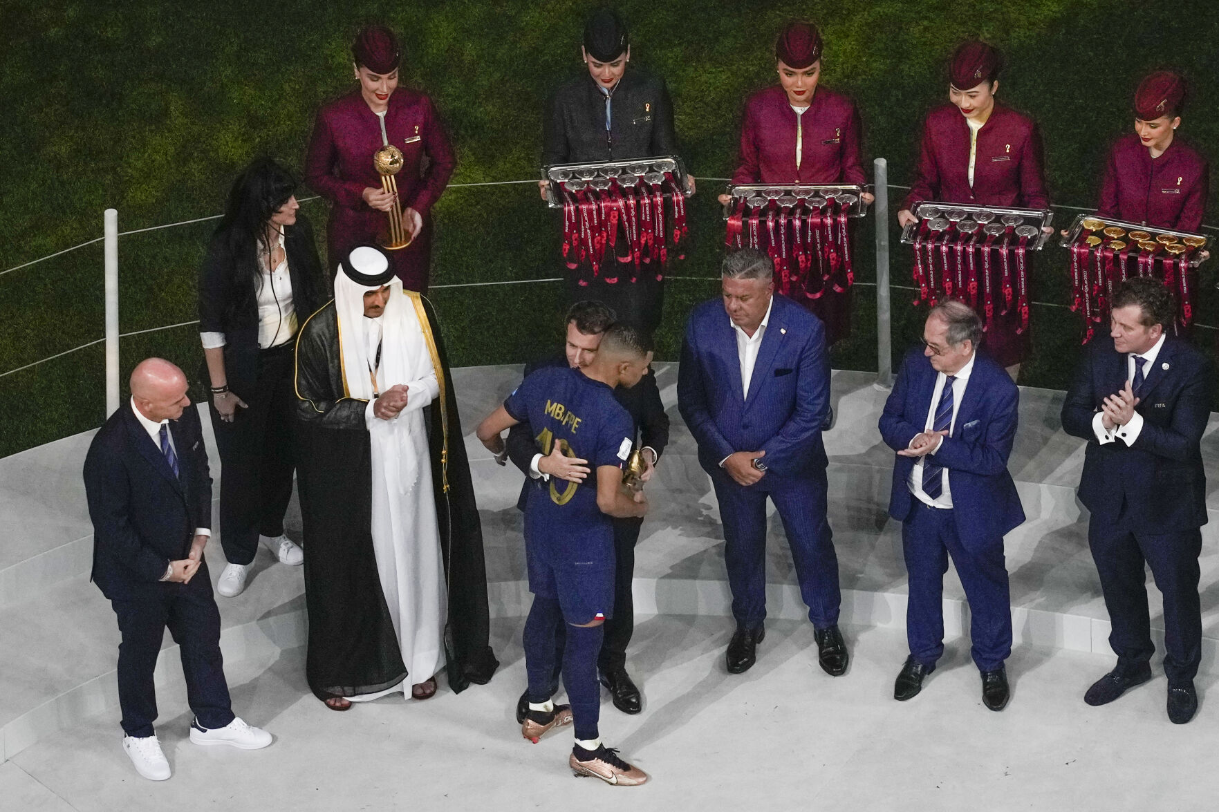 FILE - Qatar Airways staff in uniform, in background, assist in the medal ceremony, as French President Emmanuel Macron hugs France