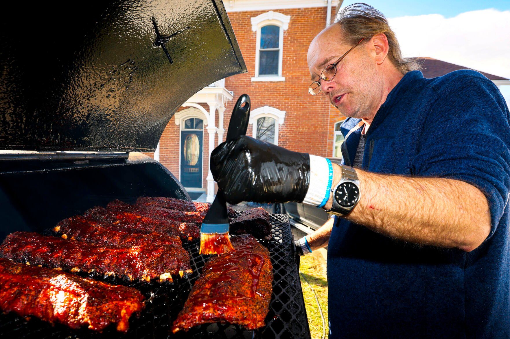 James Frank, owner of Bad Ash BBQ in Bellevue, brushes sauce over racks of ribs as they smoke, for his grand opening on Thursday, Feb. 8.    PHOTO CREDIT: Thomas Eckermann