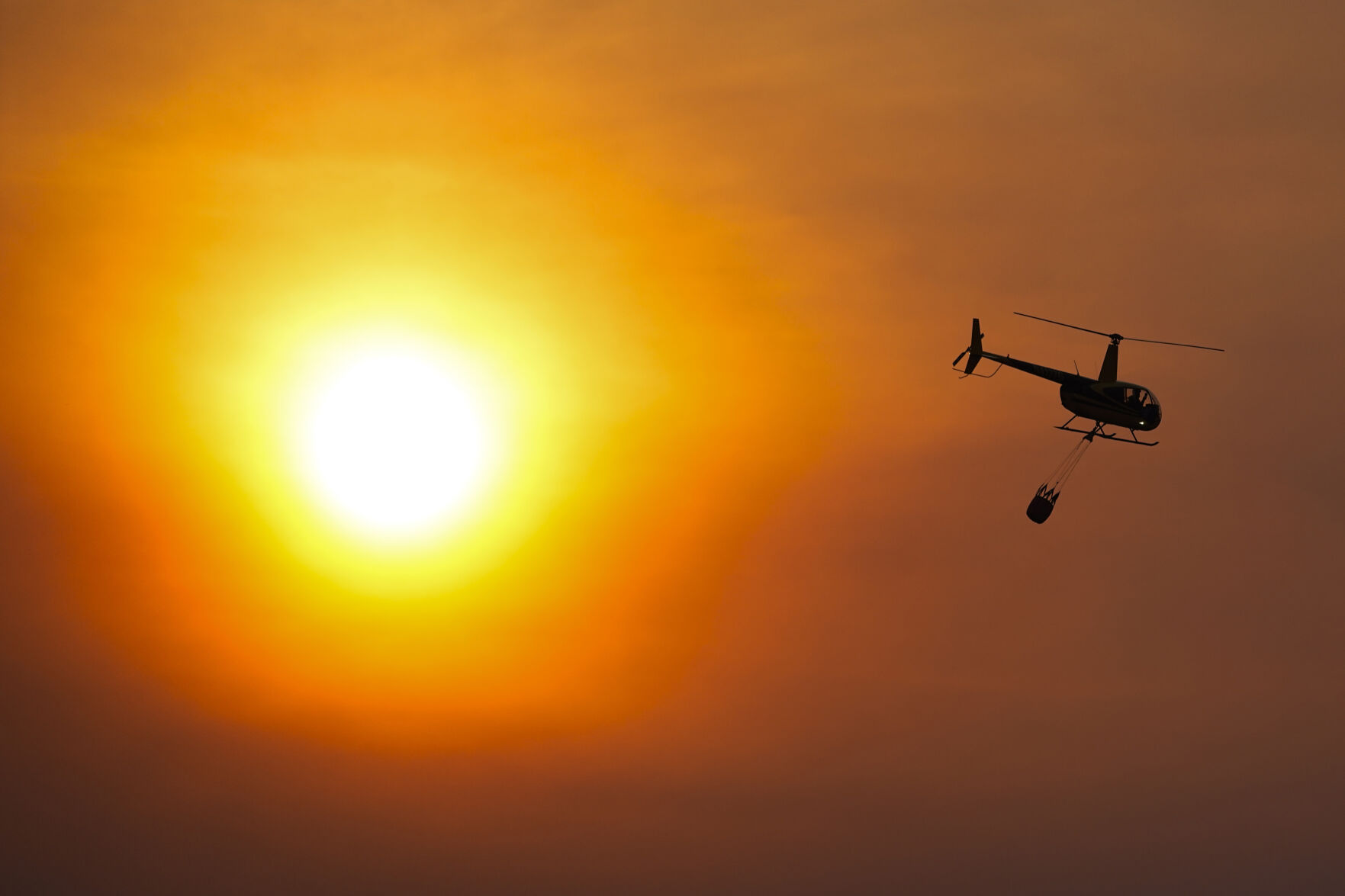 A helicopter carries a bucket as it flies over homes burned by the Smokehouse Creek Fire, Wednesday, Feb. 28, 2024, in Canadian, Texas. (AP Photo/Julio Cortez)    PHOTO CREDIT: Associated Press