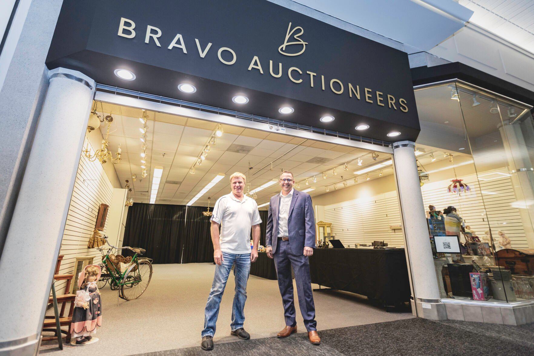 Auctioneer Tim Markham (right) stands with auction coordinator Kraig Ney at the entrance of Bravo Auctioneers at Kennedy Mall in Dubuque. Markham is a second-generation auctioneer.    PHOTO CREDIT: Thomas Eckermann