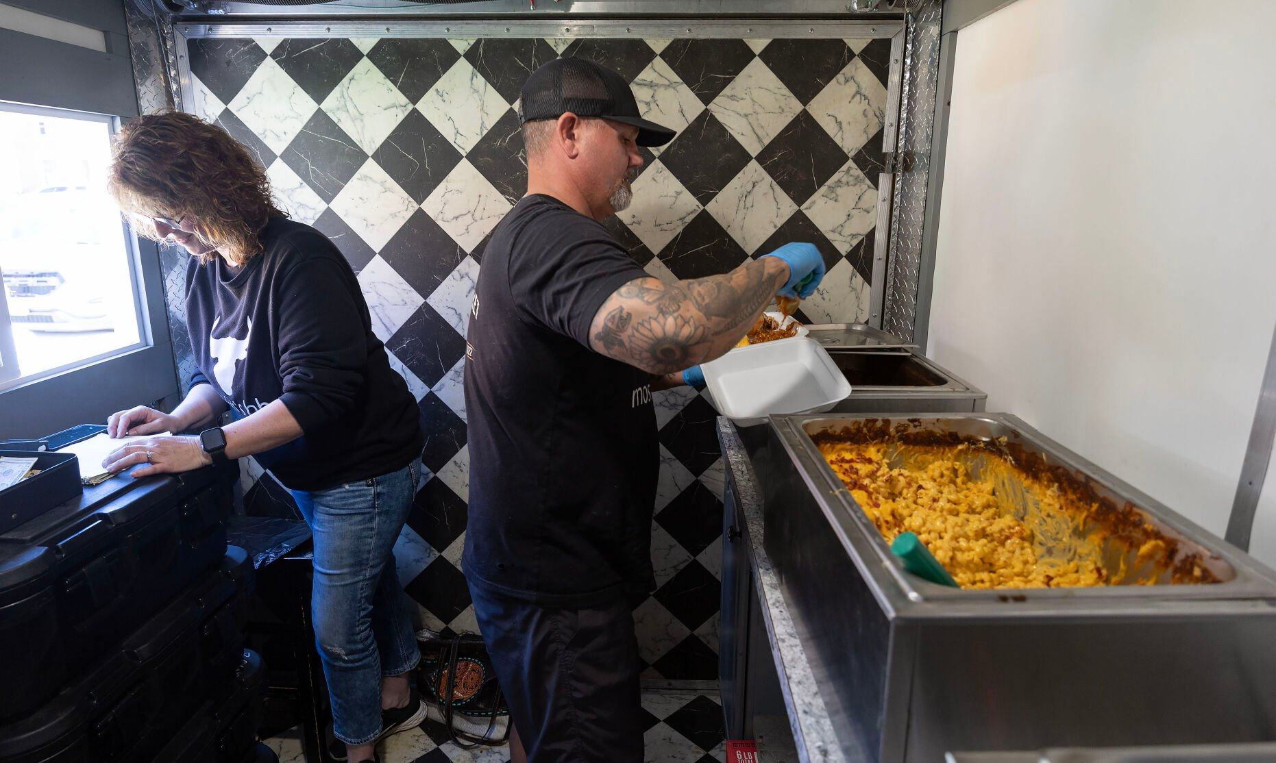 Co-owner Brice Morris prepares a sandwich while Staci Fritz rings up a sale inside Moski’s BBQ food truck while parked in Guttenberg, Iowa, last week.    PHOTO CREDIT: Stephen Gassman Telegraph Herald